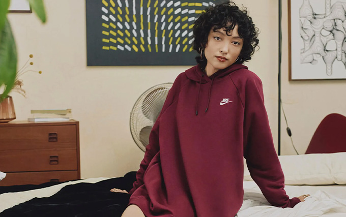 femme assise sur un lit avec un pull Nike bordeaux